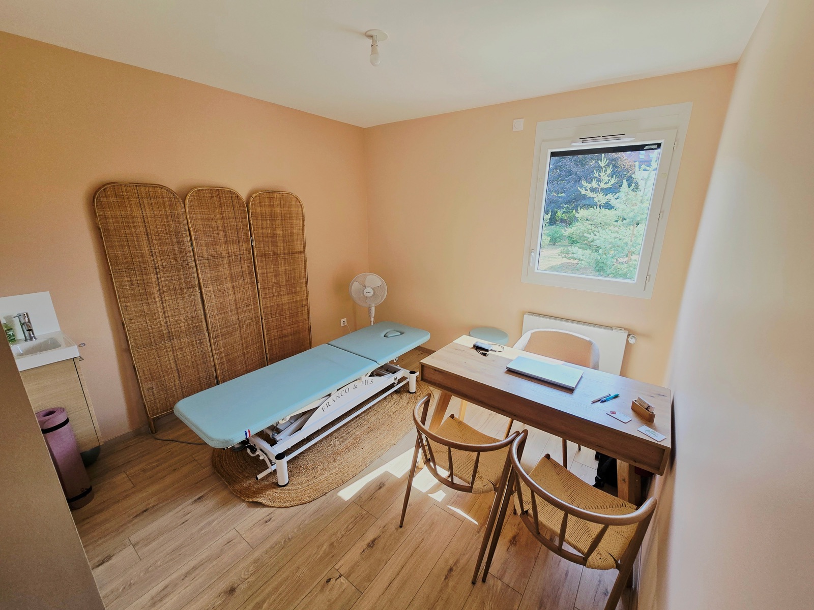 Salle de soin lumineuse avec table d’ostéopathie et paravent en rotin